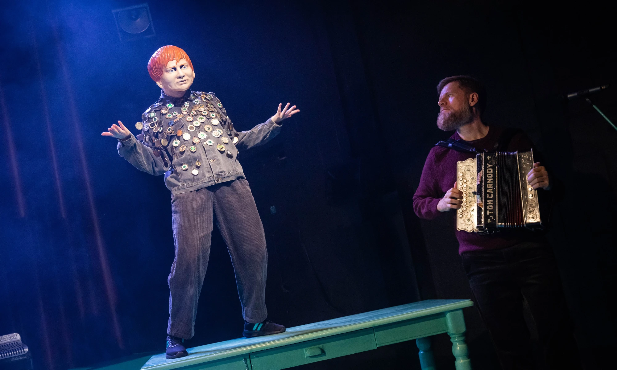 Photo from Bellow - one masked actor standing on table, the other playing the accordion