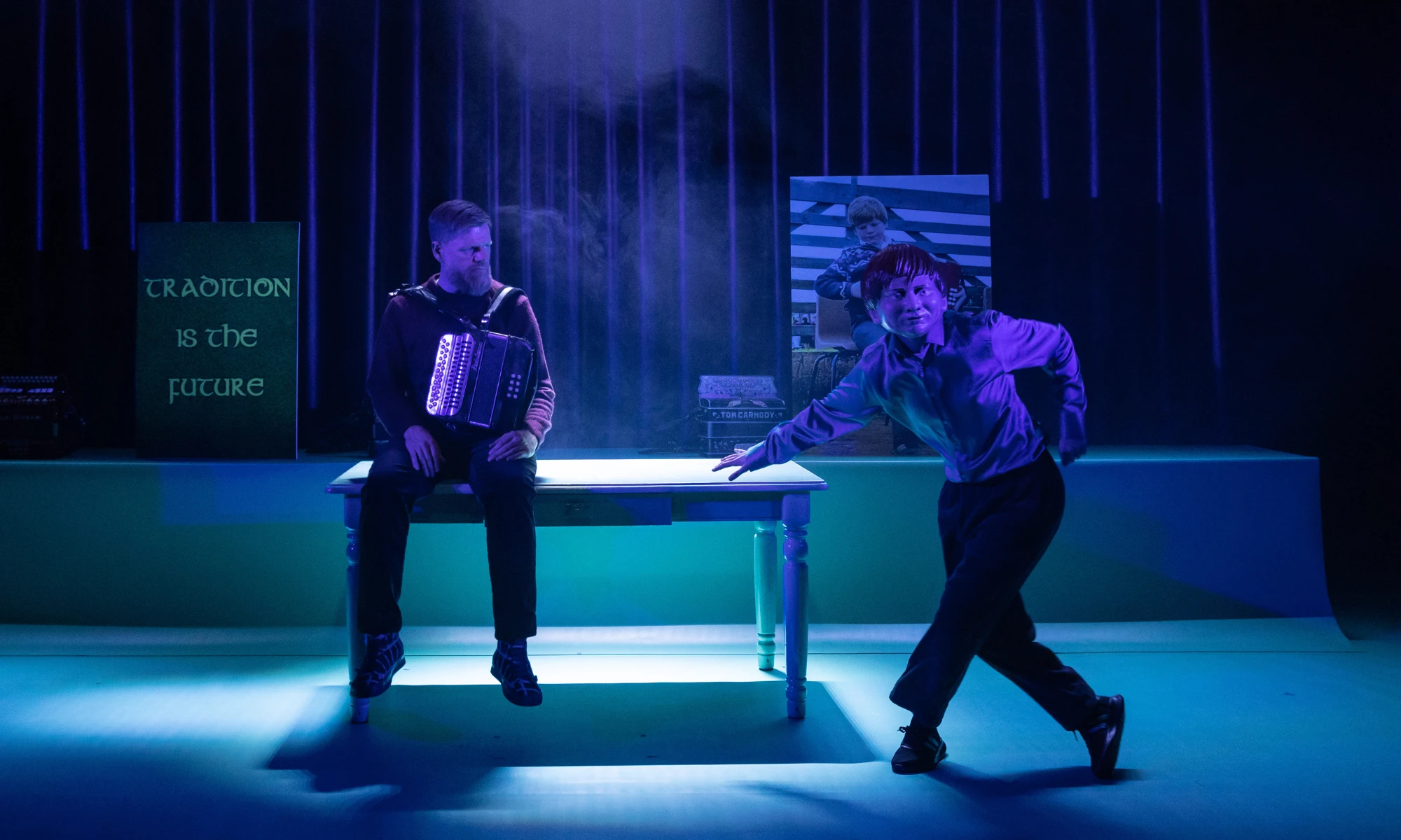 Photo of two actors from Bellow on stage - one masked and dancing. 