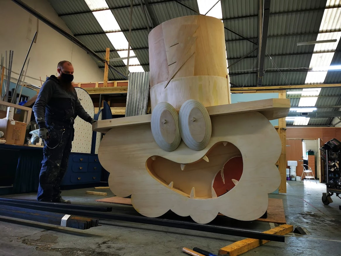 Man standing beside large-scale wooden sculpture of head with hat.