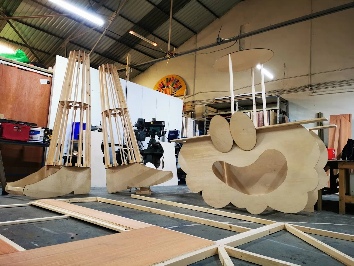 Man standing beside large-scale wooden sculpture of head with hat.