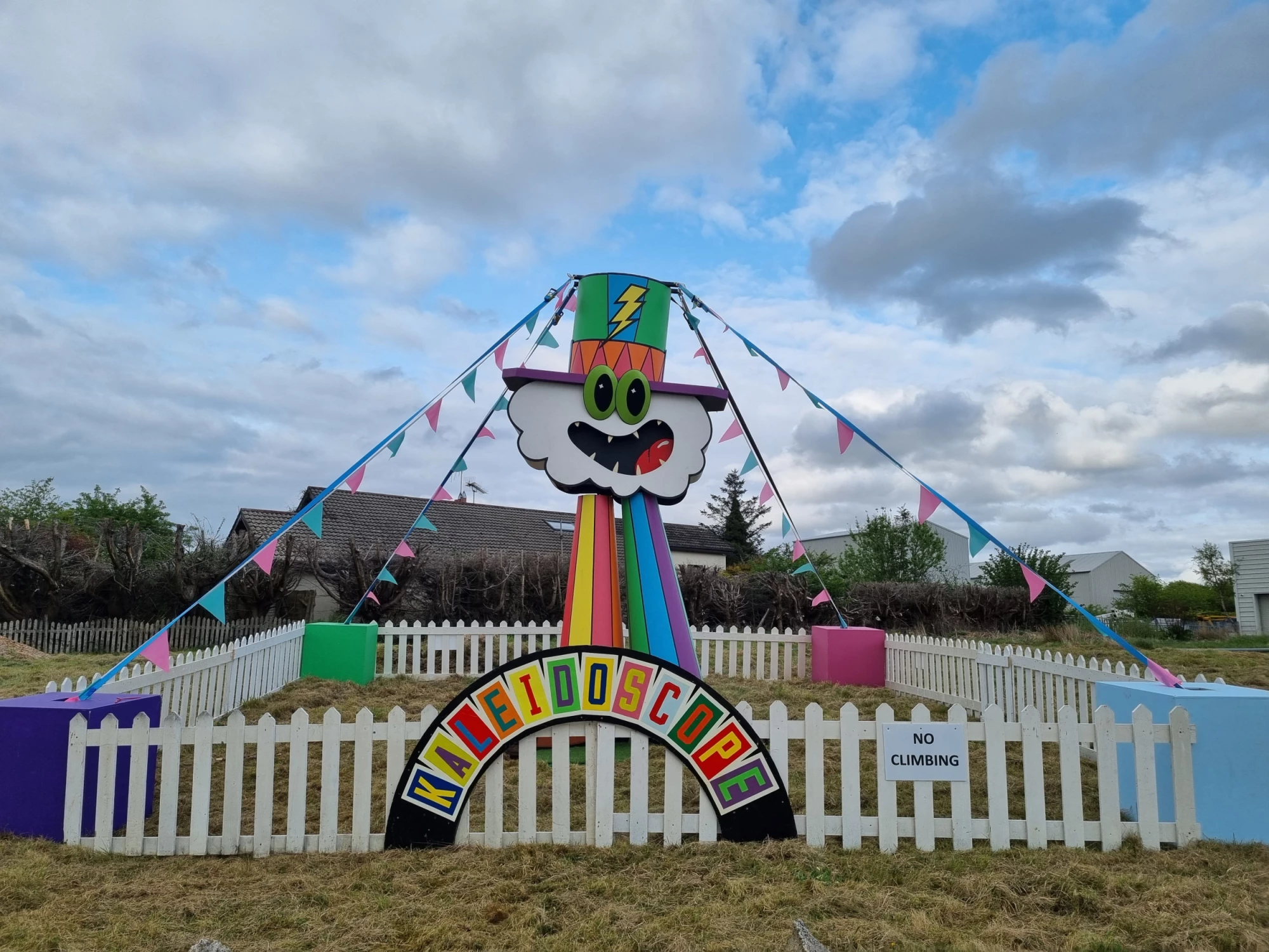 Large-scale colourful sculpture in a fenced area with bunting. 