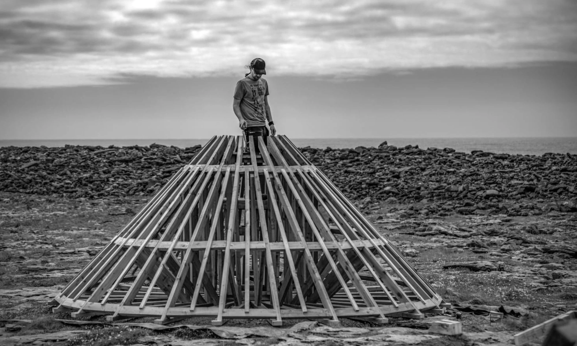 Man standing on the top of wooden conical structue in rocky landscape.