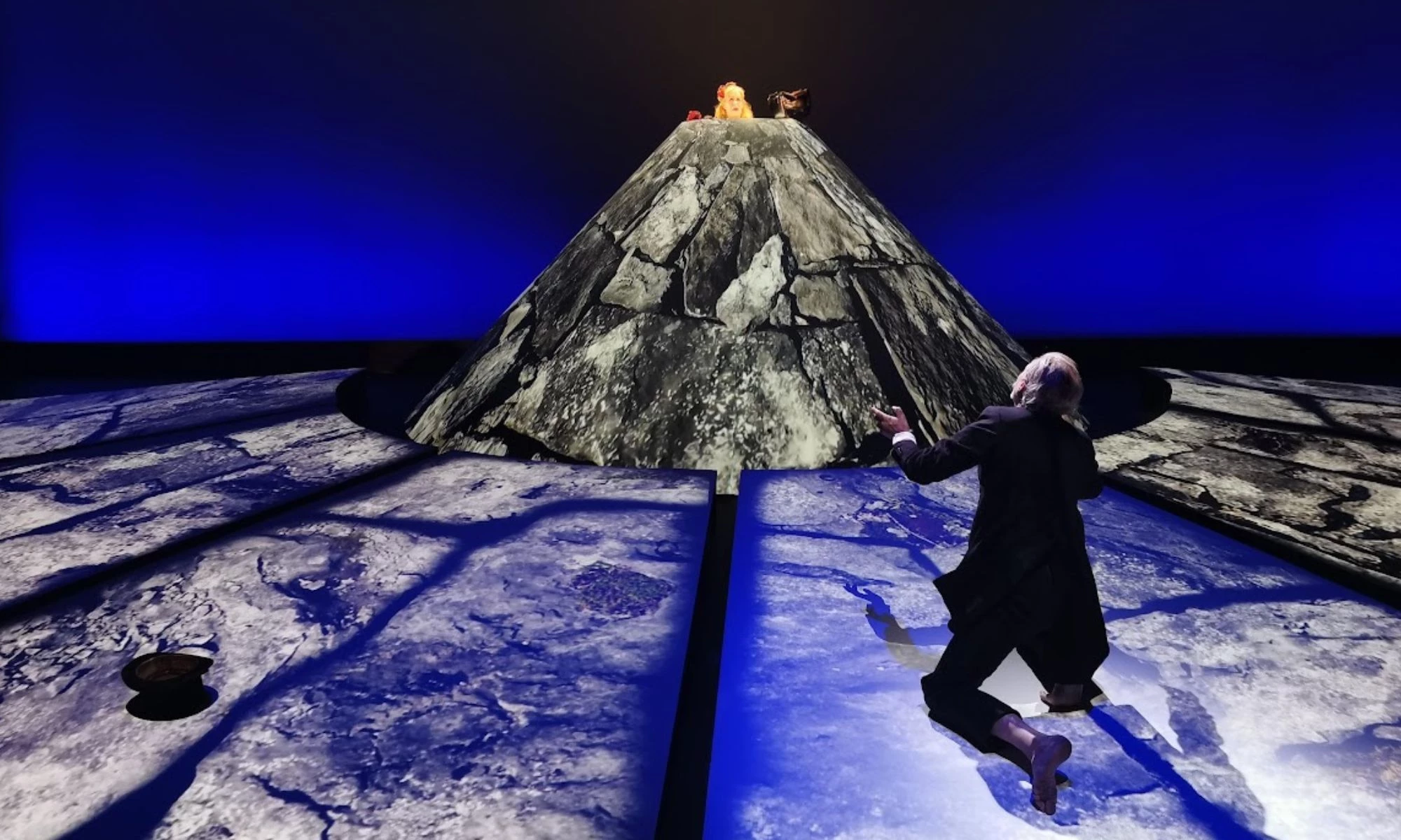 Man kneeling on projected stage looking towards female in conical rock structure.