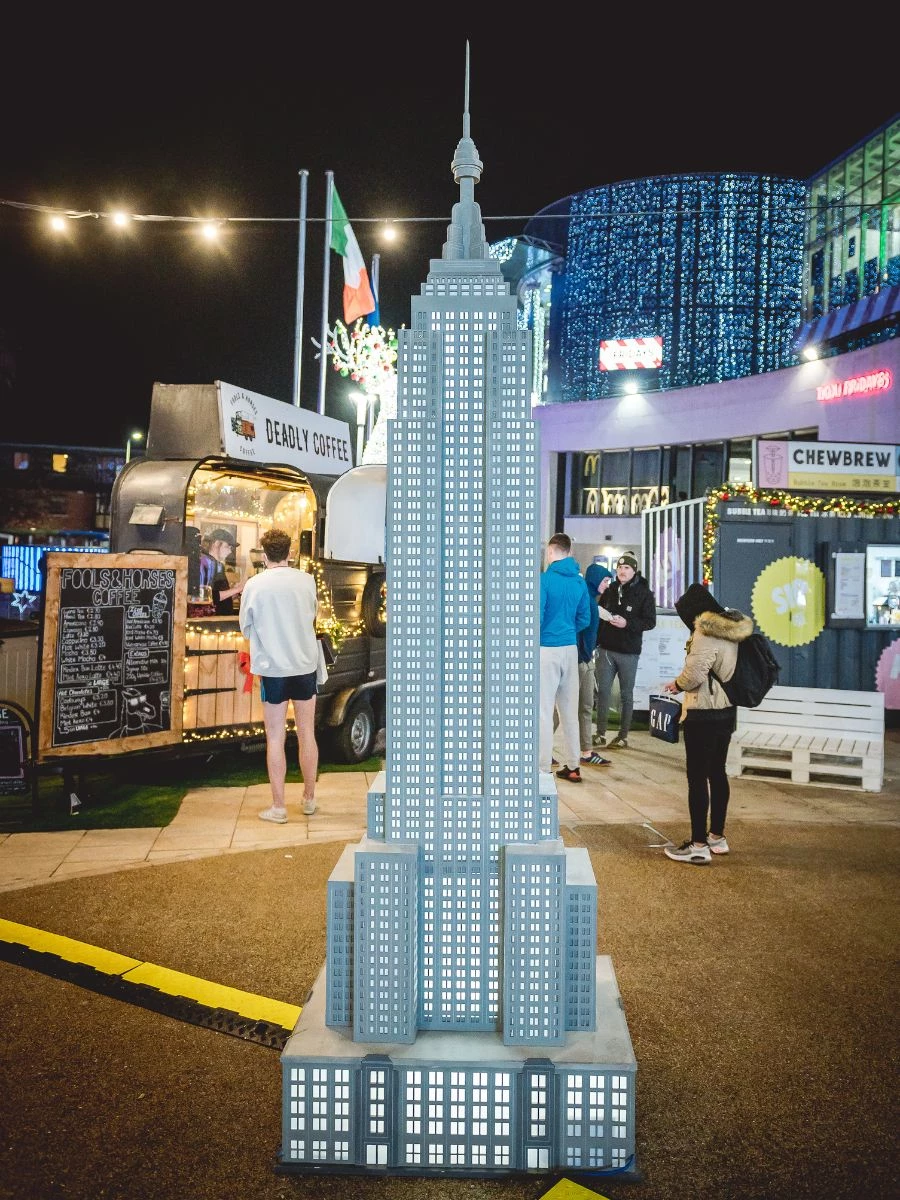 Miniature Empire State building with figures and shopping centre in background. 