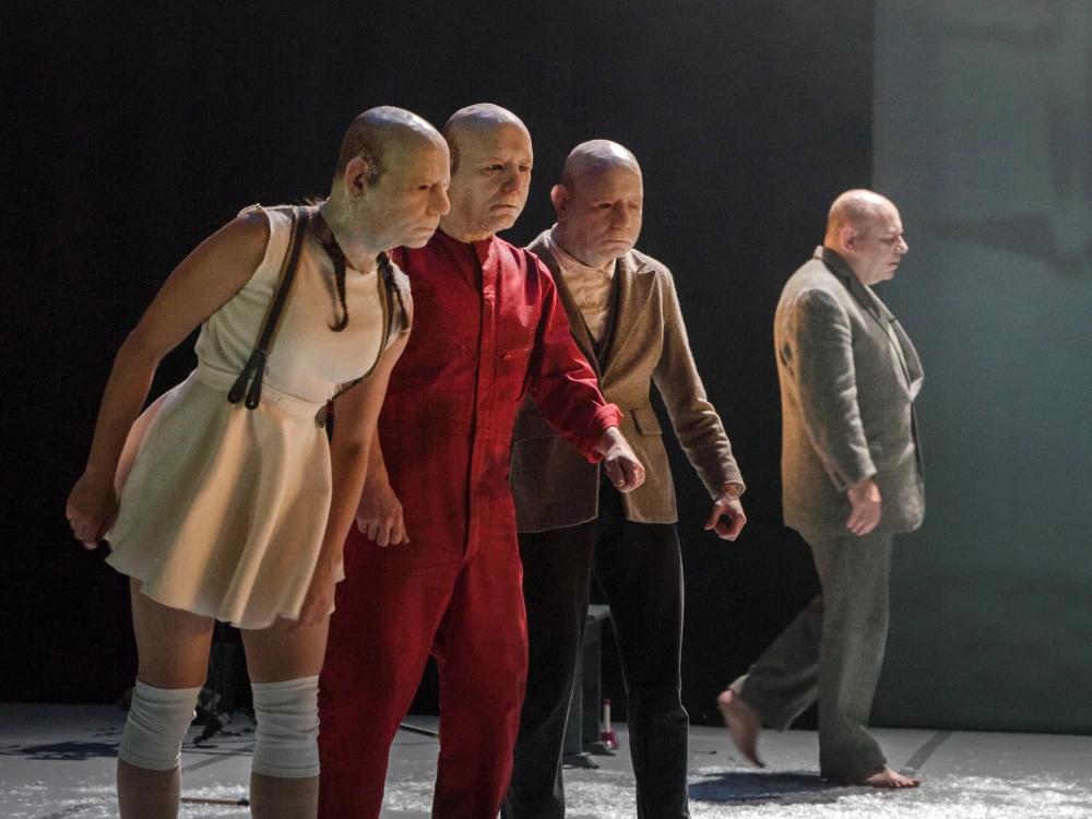 One woman and three men on stage wearing identical silicone moulded masks.
