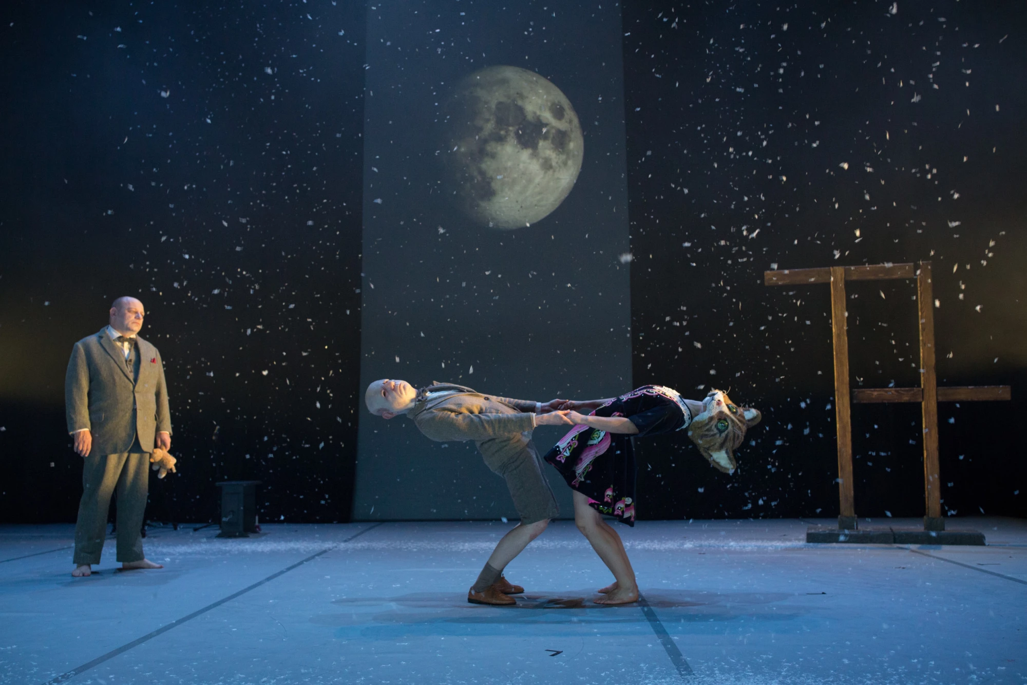 Stage set with projected moon and sky behind, two figures dancing and one figure on left. 