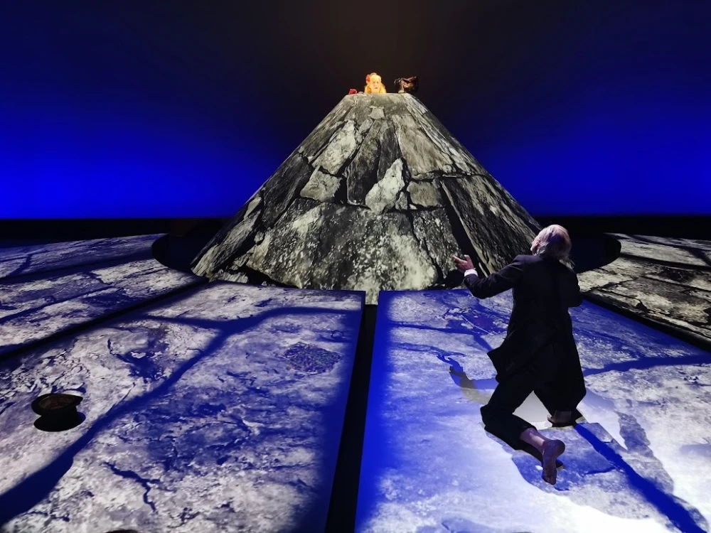 Set design of Happy Days play with man kneeling facing woman in rock formation.